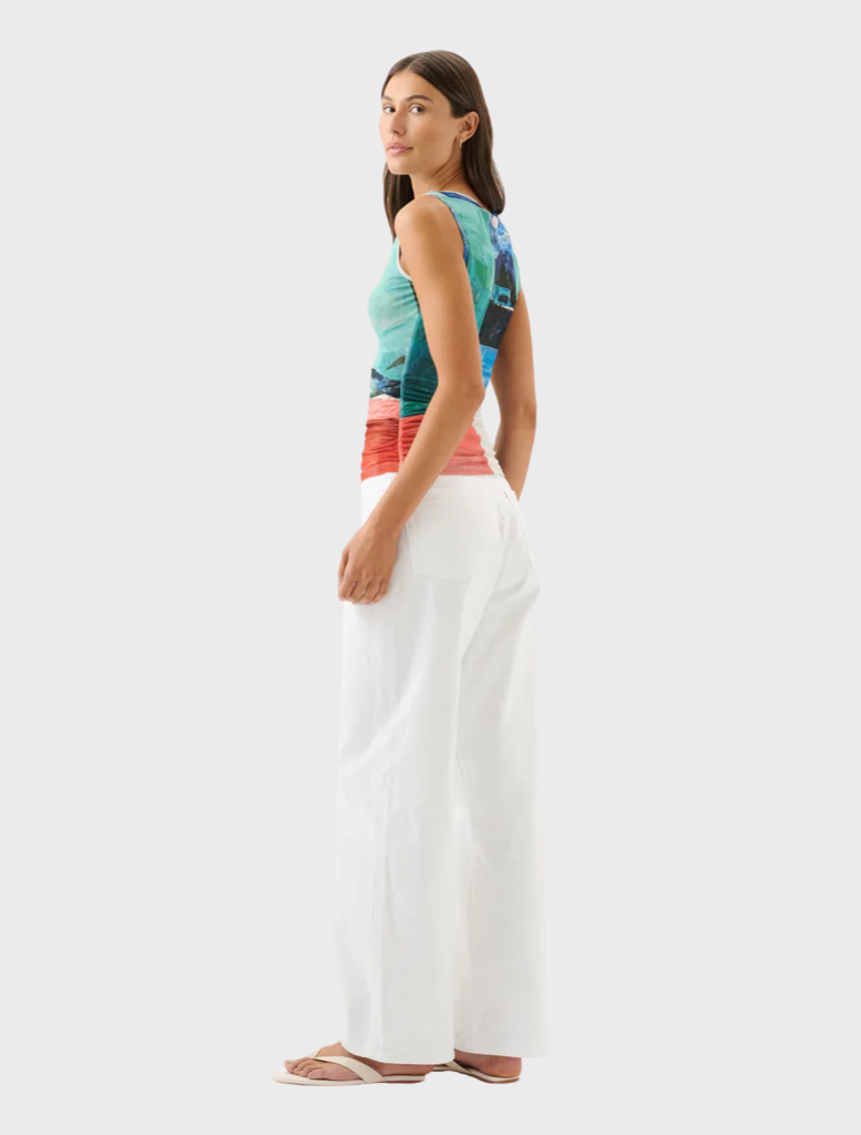A woman in white slacks and a lively, multicolored top stands, exuding a sense of style and confidence.