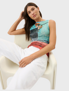A woman in white slacks and a lively, multicolored top stands, exuding a sense of style and confidence.