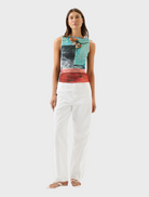 A woman in white pants and a vibrant, colorful top stands confidently, showcasing her stylish outfit.