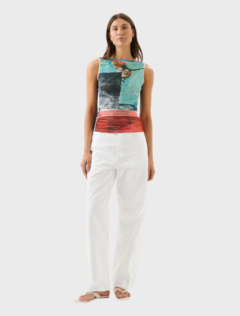 A woman in white pants and a vibrant, colorful top stands confidently, showcasing her stylish outfit.