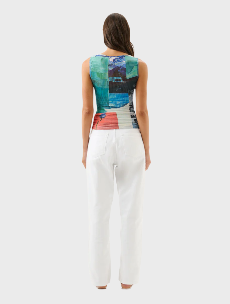 A woman showcases her outfit, featuring white pants and a strikingly colorful top, radiating fashion and flair.