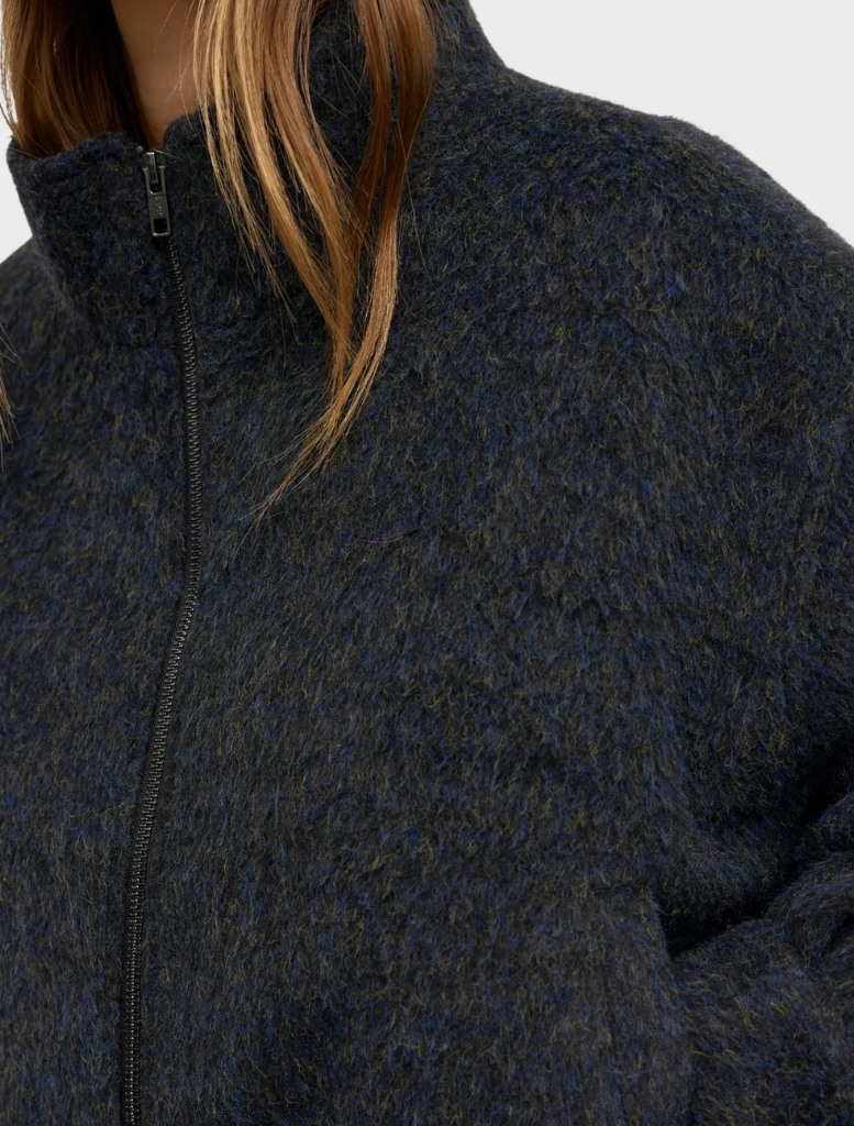 A deep ocean-colored Preslie Bomber jacket hanging, highlighting its modern cut and fabric texture.