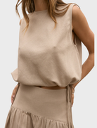 The image features a model in a tan Delphine top and skirt, presenting a fashionable ensemble.