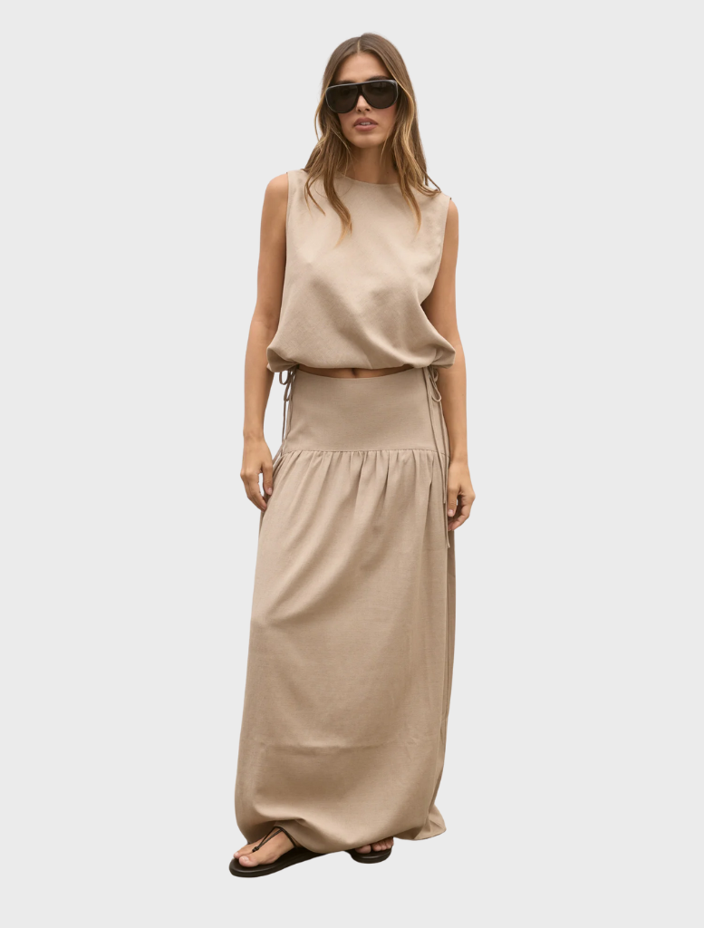 A model showcases a tan dress and sunglasses, featuring the Delphine Skirt in Nude.