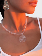 A woman wearing a brown top displays the Elara Necklace, which has a large amber stone pendant.