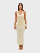 A woman wearing a pale yellow Ellis tank top and a matching skirt stands confidently, showcasing her stylish outfit.