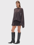 Evariel Mini Dress in Truffle features a boat neckline, sheer upper, voluminous sleeves, and a flared mini skirt with criss-cross straps.