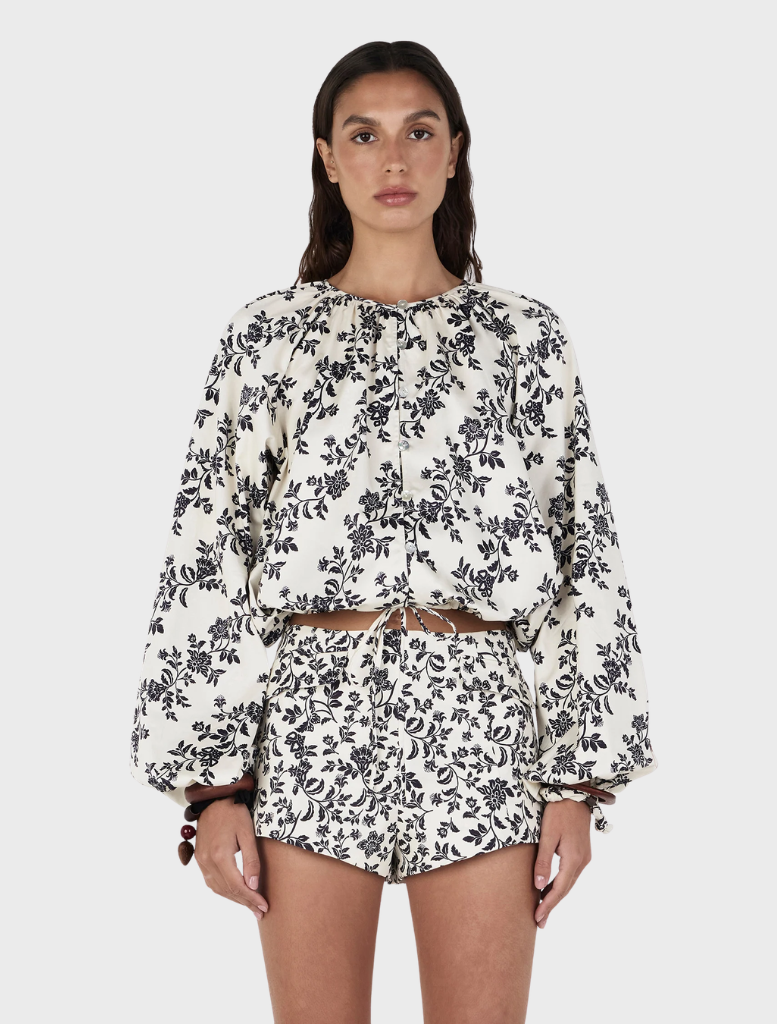 A model showcases the Felix Blouse – Moonlit Vine, wearing a white and black floral print top with matching shorts.