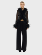 Model wearing a black Gigi Feather Blouse adorned with feathers, showcasing a stylish and elegant design.