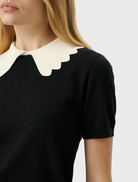 Sophisticated black knit top featuring a body-hugging fit, short sleeves, and a playful scalloped collar.
