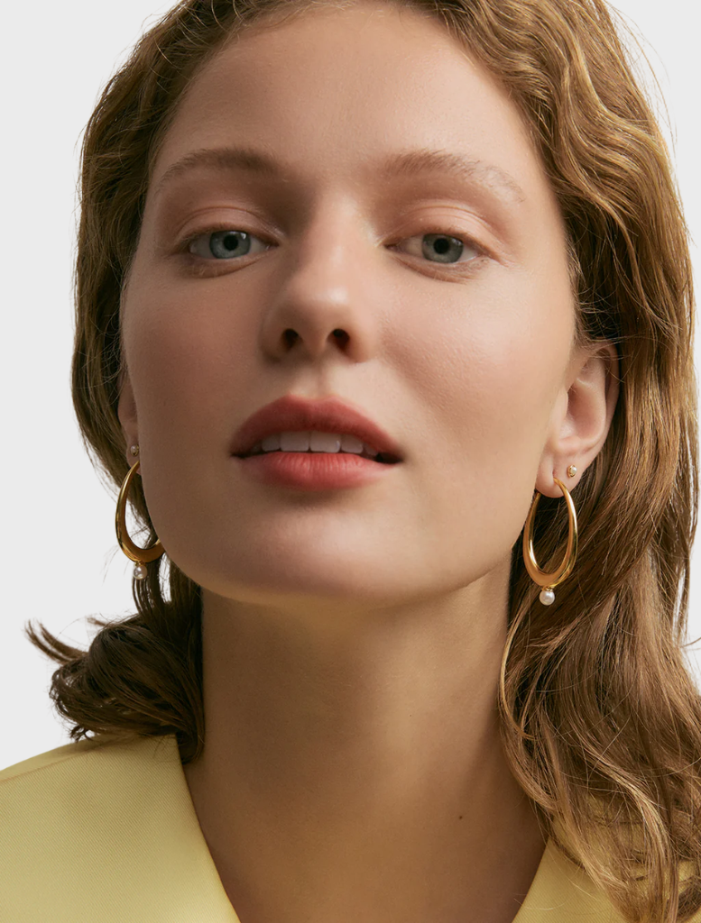 A pair of gold Pippa hoops earrings, featuring a sleek and modern design, resting on a soft surface.