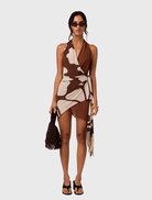 Isola Wrap Mini Dress in Ibisco features a plunging halter neck, wrap closure, and asymmetric handkerchief hem with floral print.