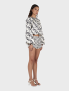 A model wears a floral print top in white and black, complemented by Jacques Shorts in the Moonlit Vine pattern.