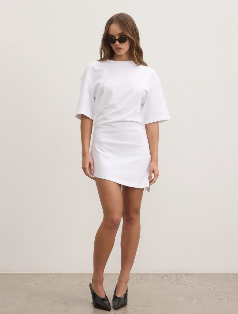 A model wearing a white t-shirt dress and sunglasses stands, highlighting a chic and relaxed fashion choice.
