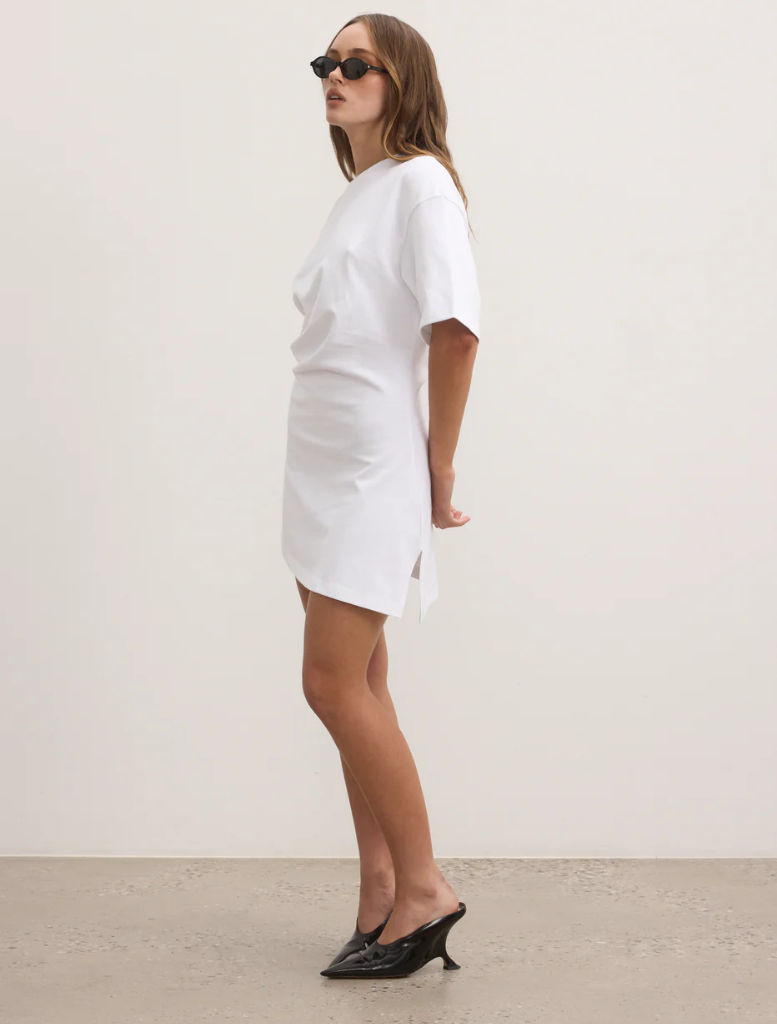 A model in a white t-shirt dress and sunglasses poses confidently against a neutral background.