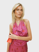 A woman in a fuchsia dress holds an orange bag, showcasing a stylish outfit with a vibrant color contrast.