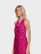 A woman in a fuchsia dress holds an orange bag, presenting a chic and colorful ensemble.