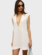 A woman in a white Juno dress and sandals poses gracefully, embodying a fresh and chic summer look.