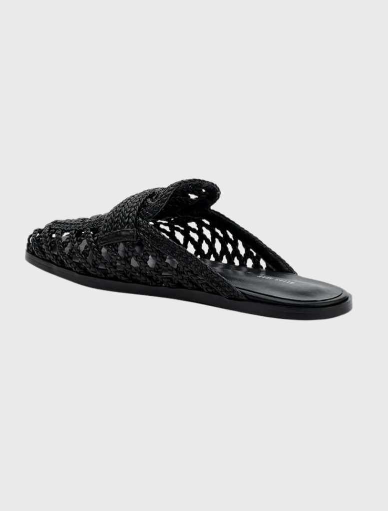 The Krissy flat mule is black, woven, and features a square toe, wide crossover strap, and an open back for easy wear.
