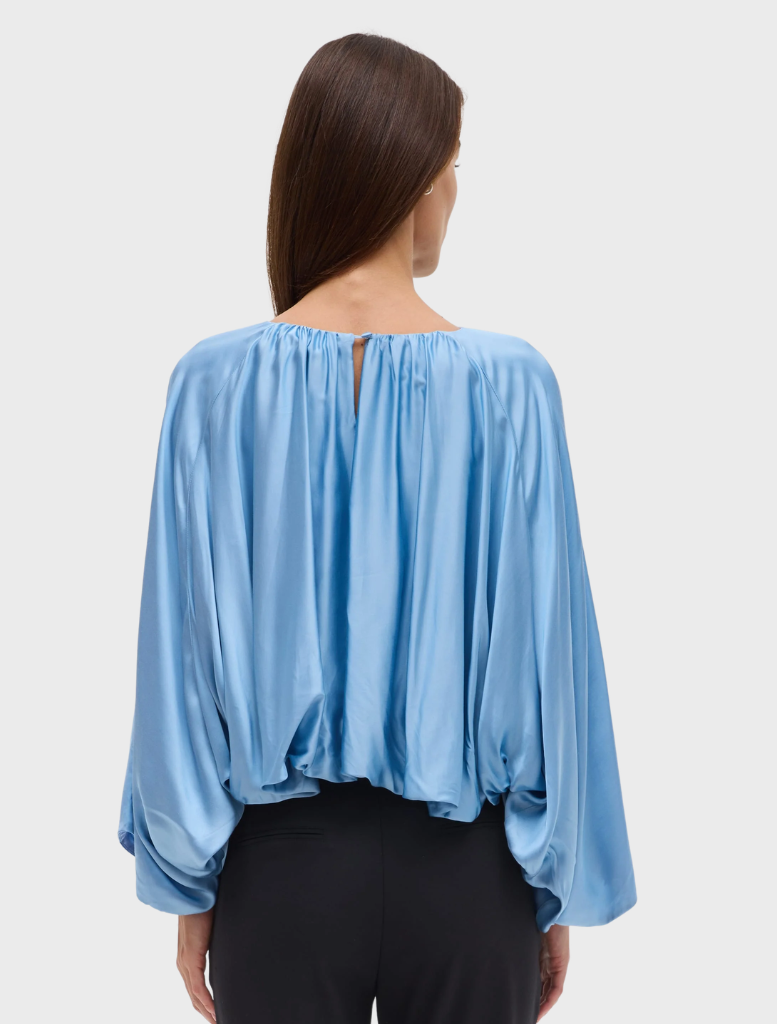 The Dreamt Blouse in lapis showcases a fluid design with gathered neckline, wide sleeves, and a softly bloused hem for comfort.