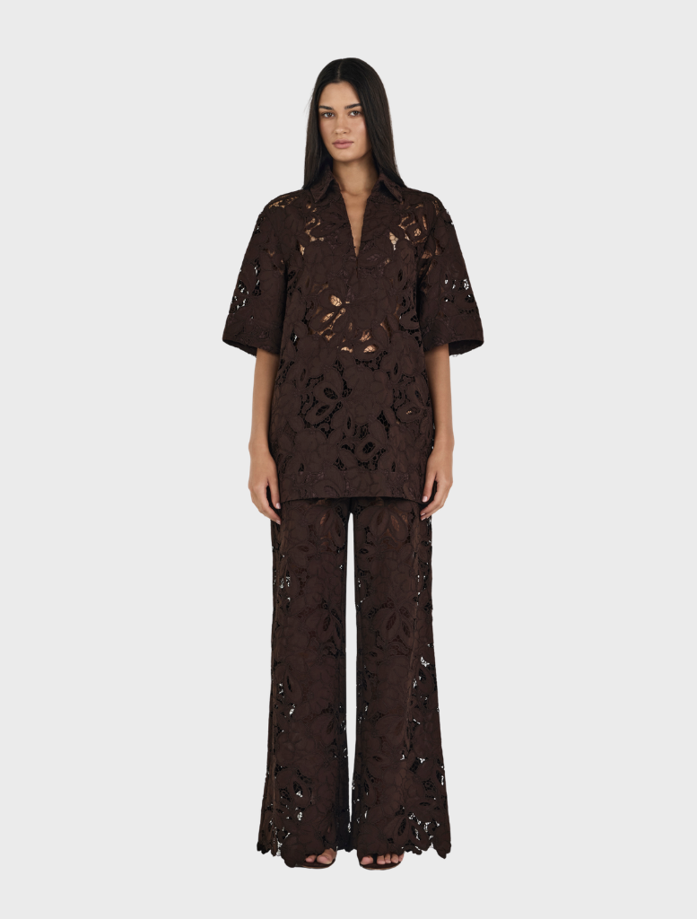 A woman in a black top and chocolate brown Lotus Lace pants poses elegantly.