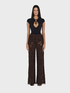 A woman wearing a black top and chocolate brown Lotus Lace pants stands confidently.
