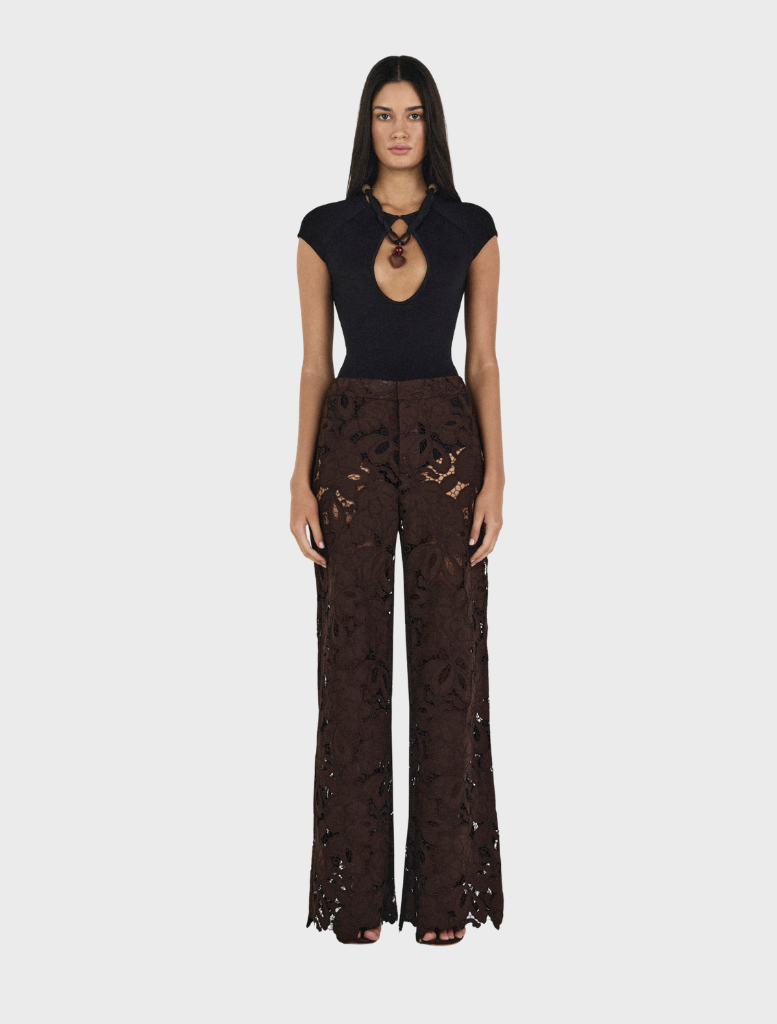 A woman wearing a black top and chocolate brown Lotus Lace pants stands confidently.