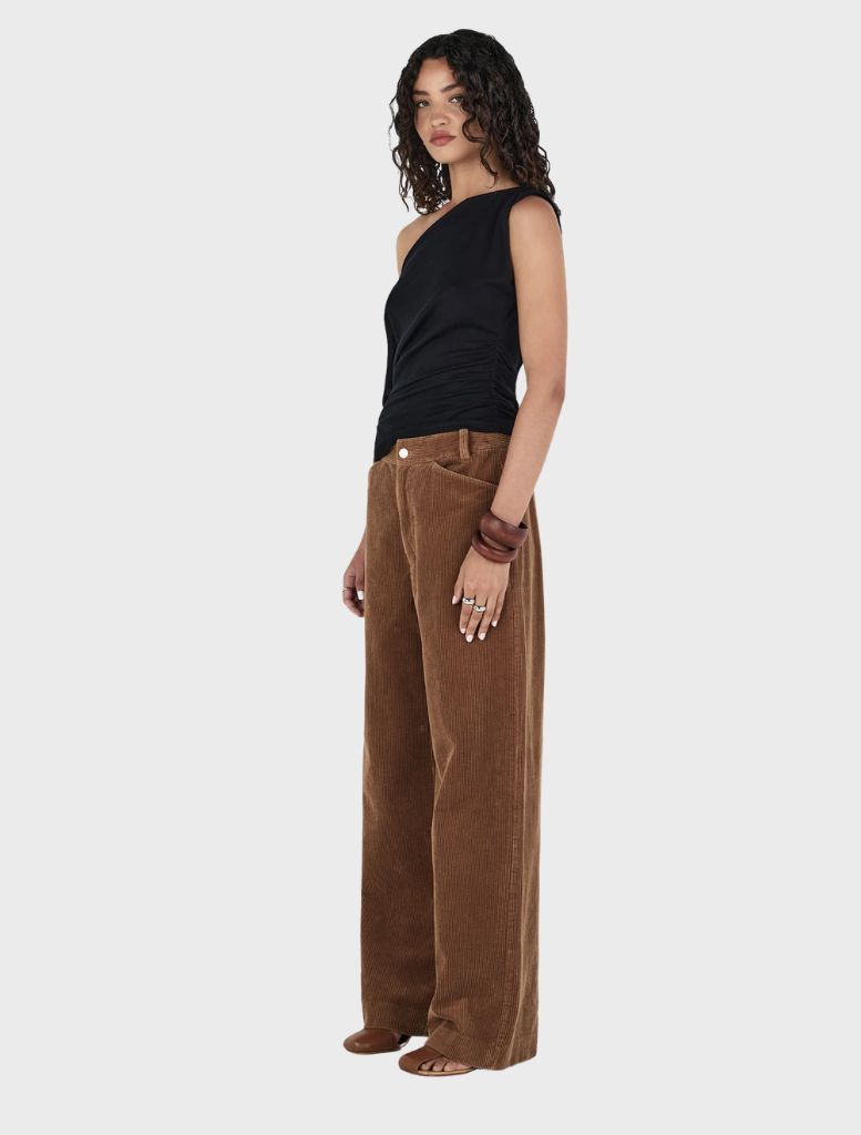 Tan Max Cord Pants draped over a chair, illustrating their casual yet sophisticated style.