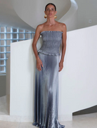 A woman in a metallic dress poses elegantly on a stairway, showcasing her stylish outfit and confident demeanor.