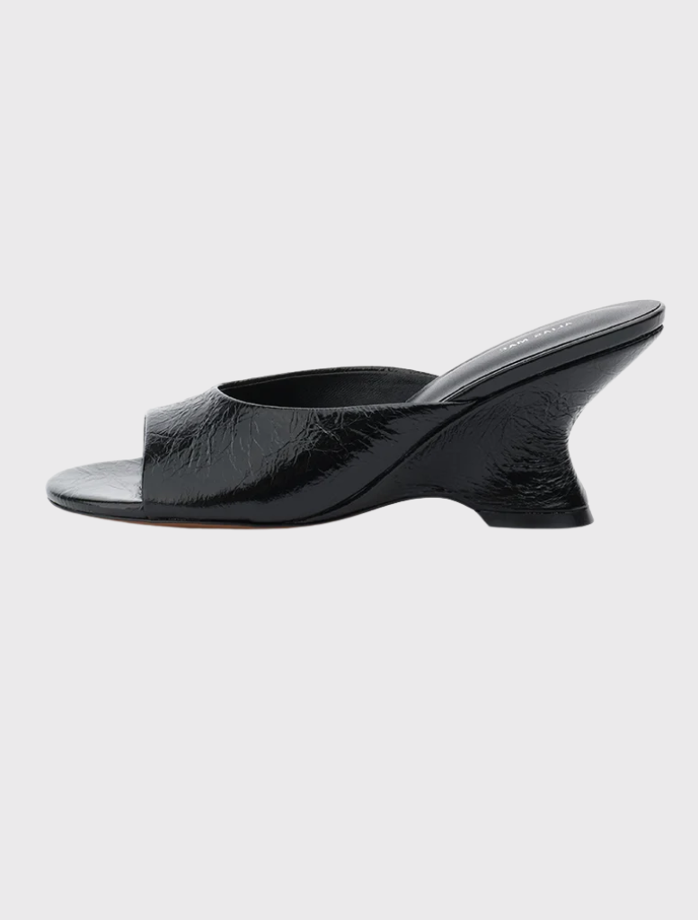 Open-toe black leather mule with wide strap and sculptural wedge heel, featuring a slip-on design and round toe shape.