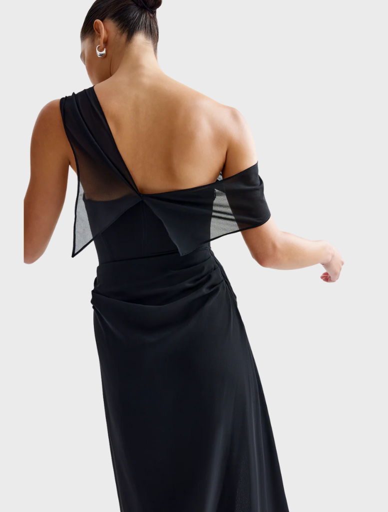 A woman dressed in black stands beside a classic car, merging contemporary fashion with timeless automotive design.