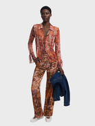 Model wearing a long-sleeve orange and brown paisley print blouse, showcasing a vibrant multi-colored design.