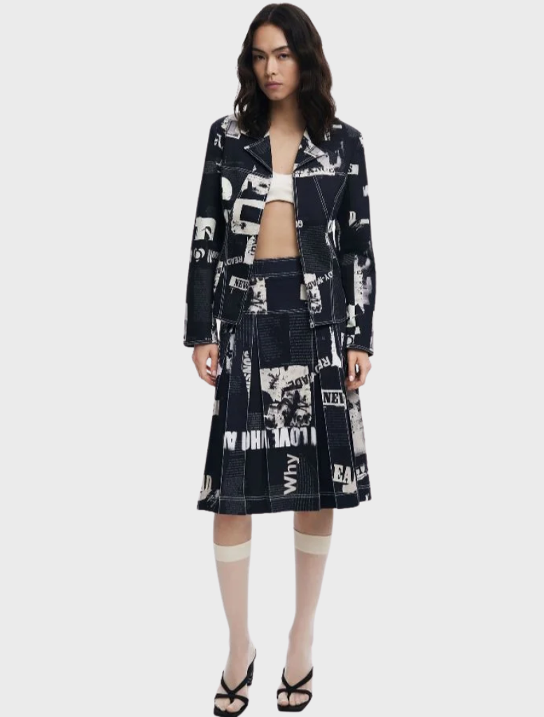 Model showcases a black and white printed skirt and jacket, featuring the Newspaper Pleated Midi Skirt in black.