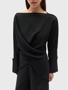 Black Novalyn Top showcasing a boat neckline, draped crossover, self-tie waist, relaxed fit, long sleeves, and wide cuffs.