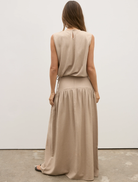 Back view of a woman in a tan dress, showcasing the Delphine Skirt in Nude.