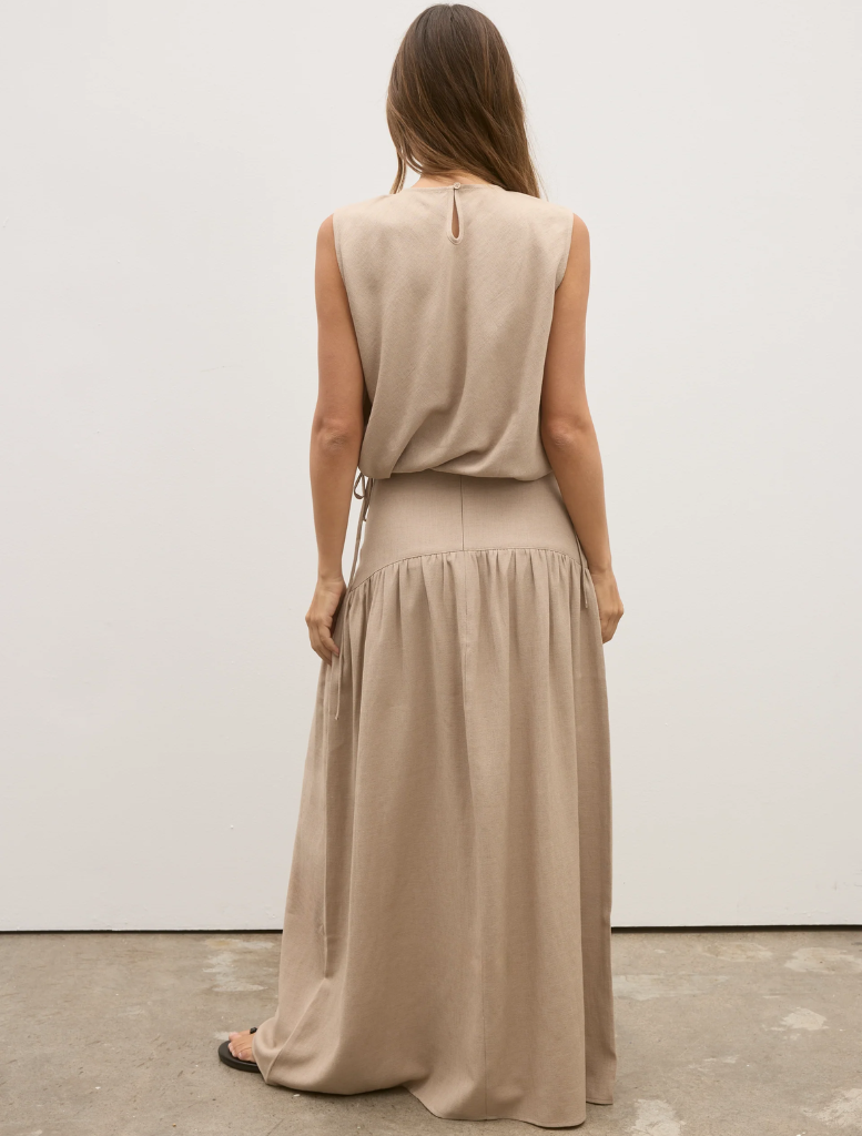 Back view of a woman in a tan dress, showcasing the Delphine Skirt in Nude.