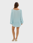 The image features a model in a pale blue romper with cutouts, identified as the Penelope Blouse.