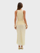 A woman dressed in a pale yellow Ellis tank top and skirt smiles, embodying a vibrant and stylish summer look.