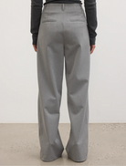 Back view of a woman wearing grey trousers, showcasing a stylish and modern outfit.