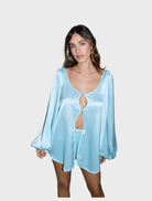 A model displays the Penelope Blouse, a pale blue romper featuring trendy cutouts.