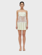 A fitted lace mini dress in lemonade color, featuring rouleau straps and a flared skirt, with a side closure for support.