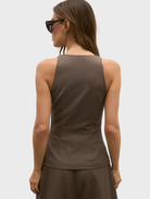 Back view of a woman in a brown Reeve Halter Top and black pants, showcasing a stylish and casual outfit.