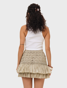 A natural Riley Raffia Skirt hanging on a rack, featuring a woven texture and a stylish, casual look.