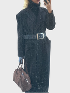 A woman in a navy blue coat and hat captures a selfie, showcasing her cheerful expression.