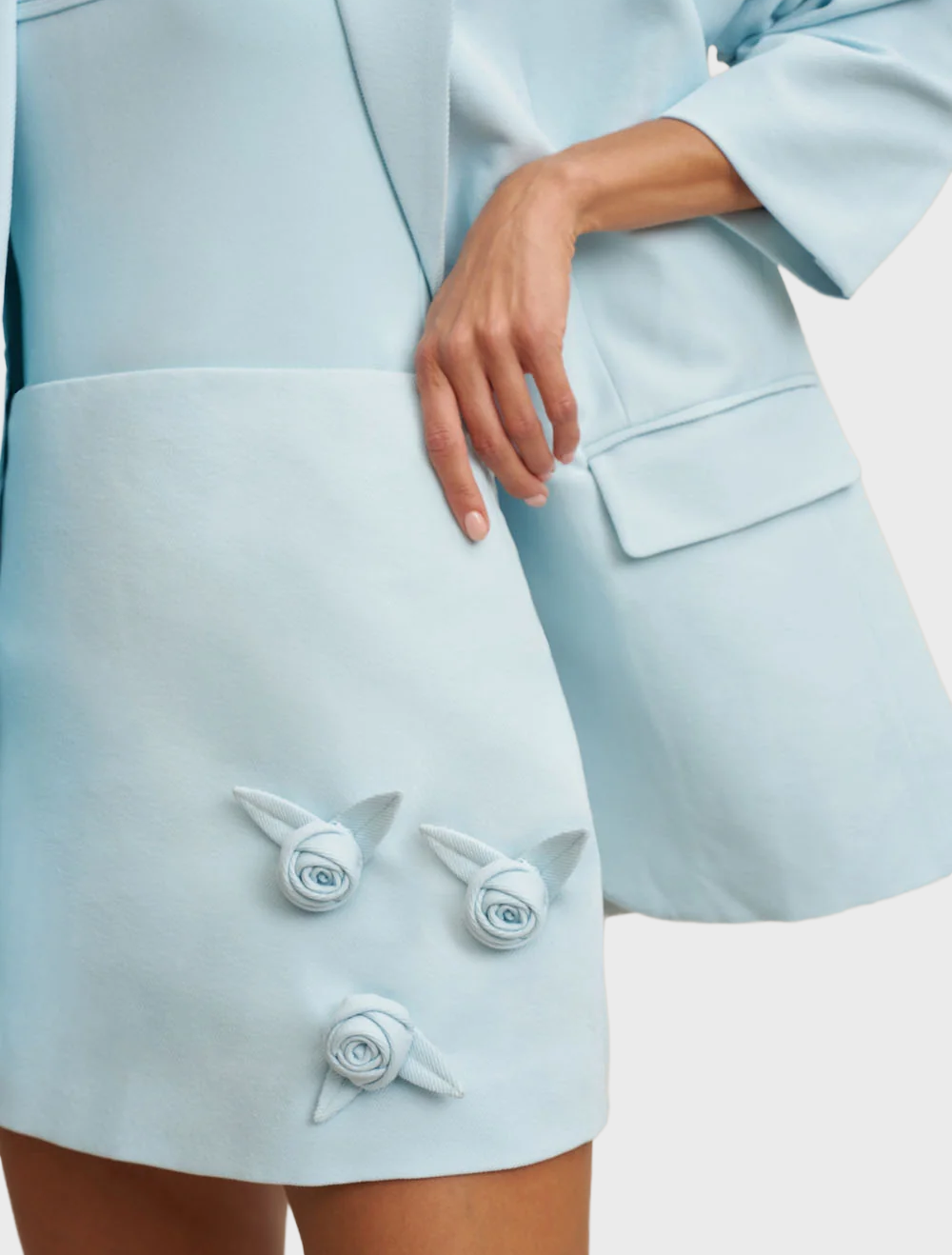 A-line mini skirt in ice blue with decorative handmade rosettes, made from structured twill and fully lined for comfort.