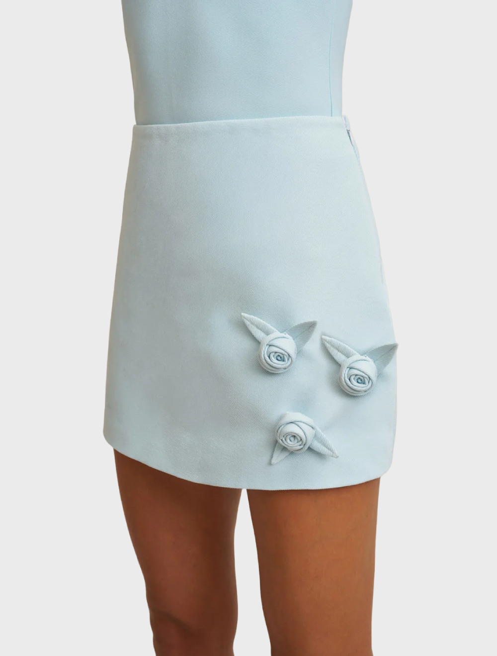 Ice blue A-line mini skirt with carefully placed handmade rosettes, made from structured twill weave and fully lined.