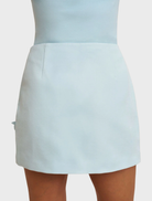 A-line mini skirt in ice blue, showcasing handmade rosettes on the front, constructed from structured twill and fully lined.