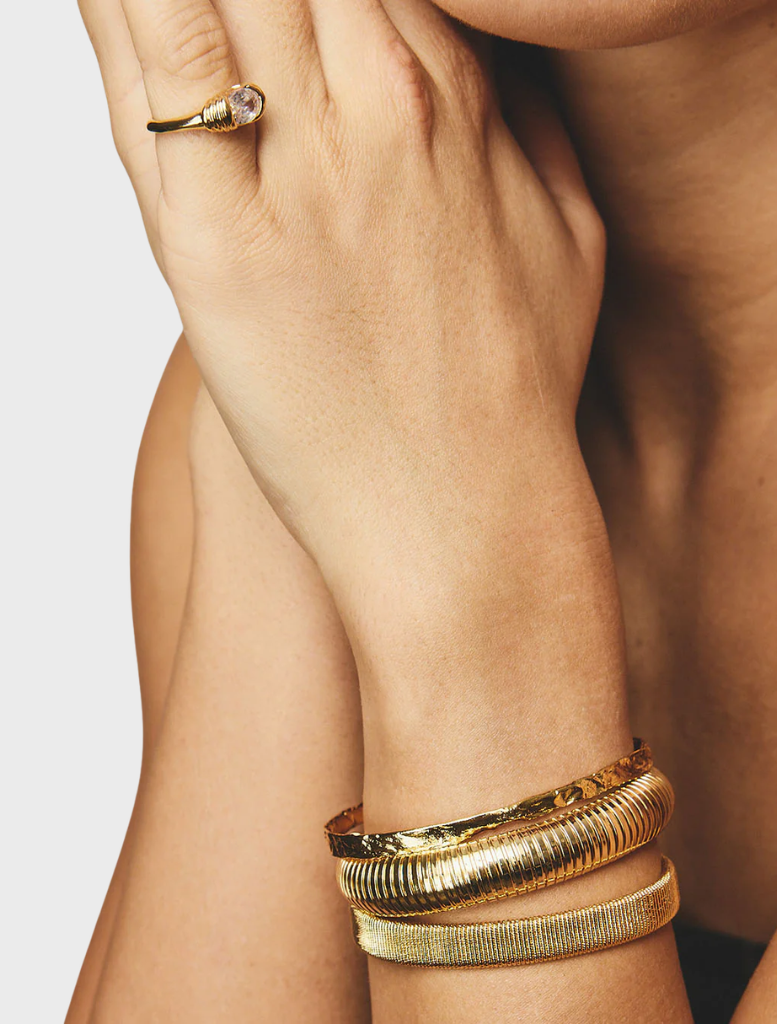Elegant gold cuff by Sabrina, featuring a minimalist design that highlights its luxurious finish.
