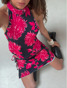 A woman in a vibrant floral dress takes a selfie, showcasing her joyful demeanor in a sunny outdoor setting.