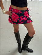 A woman wearing a floral dress poses for a selfie, capturing her cheerful expression against a natural backdrop.
